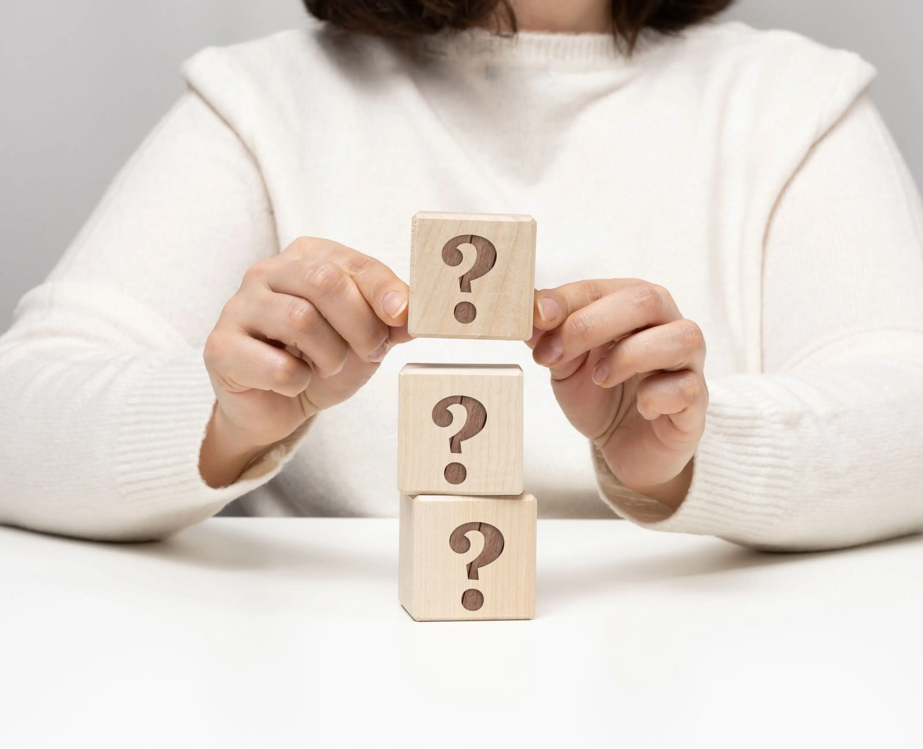 mano femenina sosteniendo un cubo de madera con un signo de interrogación, concepto de preguntas más frecuentes sobre la terapia.